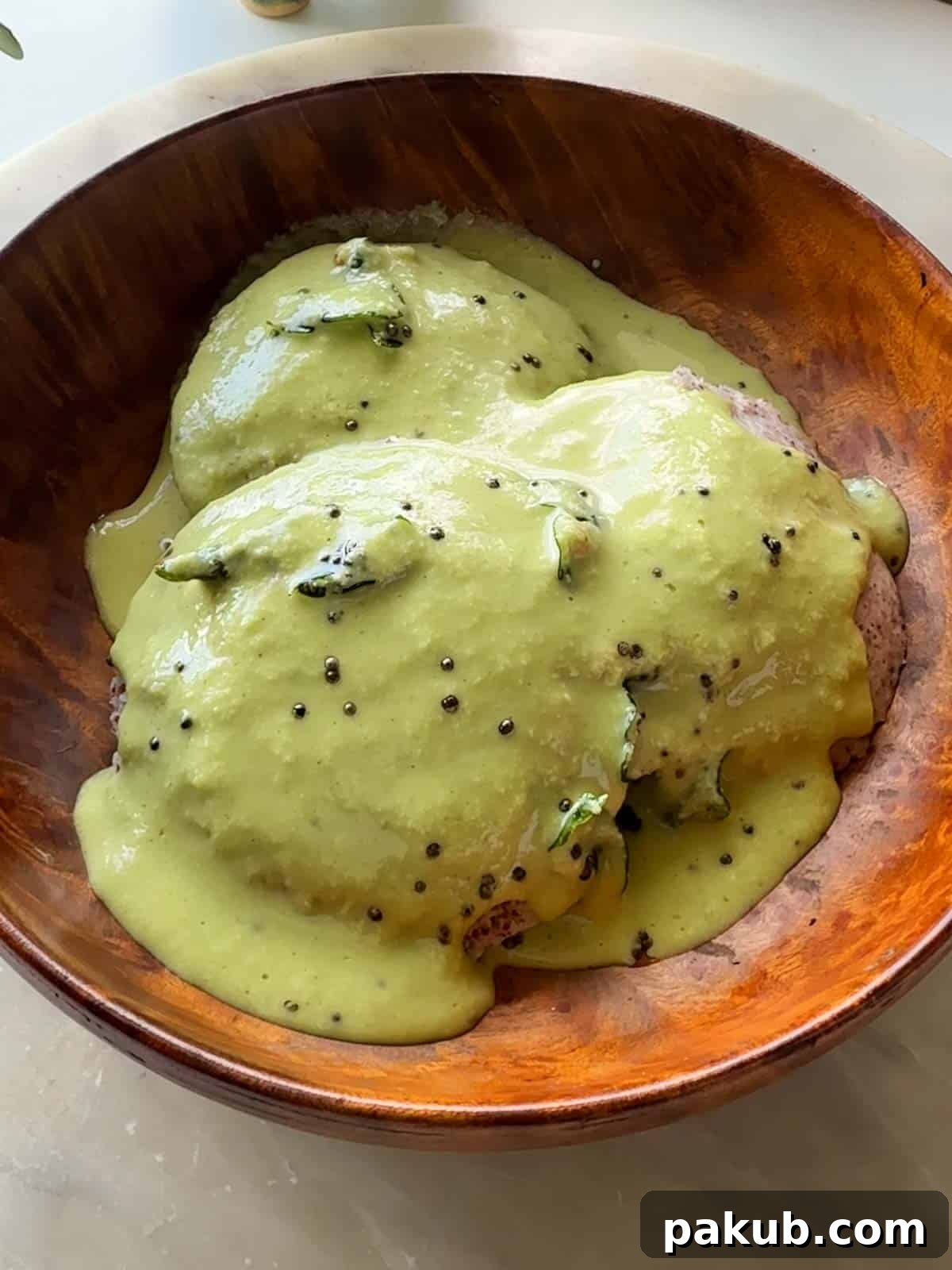 Healthy Ragi Millet Idli Dosa Batter 6 an an image of ragi idlis with chutney poured over and served in a wooden bowl