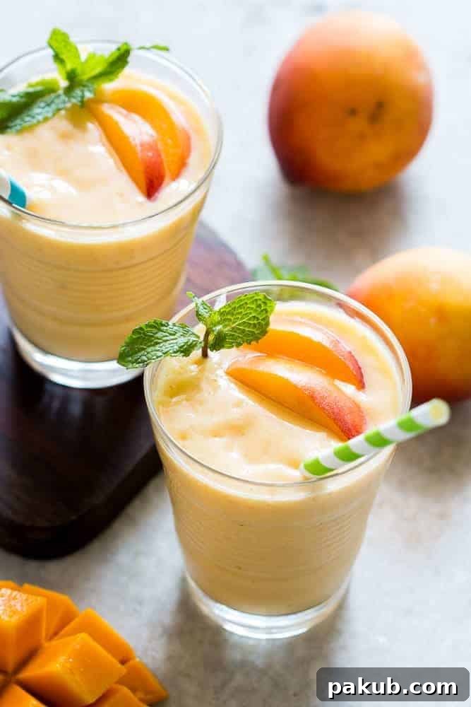 A vibrant and thick healthy vegan frozen peach mango smoothie, garnished with fresh mint, highlighting its creamy texture.