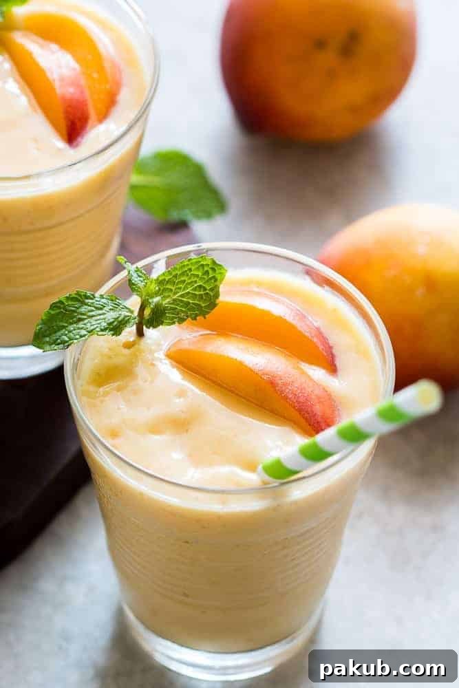 Two glasses of healthy vegan frozen peach mango smoothie, garnished with mint, ready to be enjoyed as a refreshing, thick, and dessert-like treat.