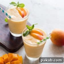Healthy Vegan Frozen Peach Mango Smoothie garnished with mint leaves and served with straws.