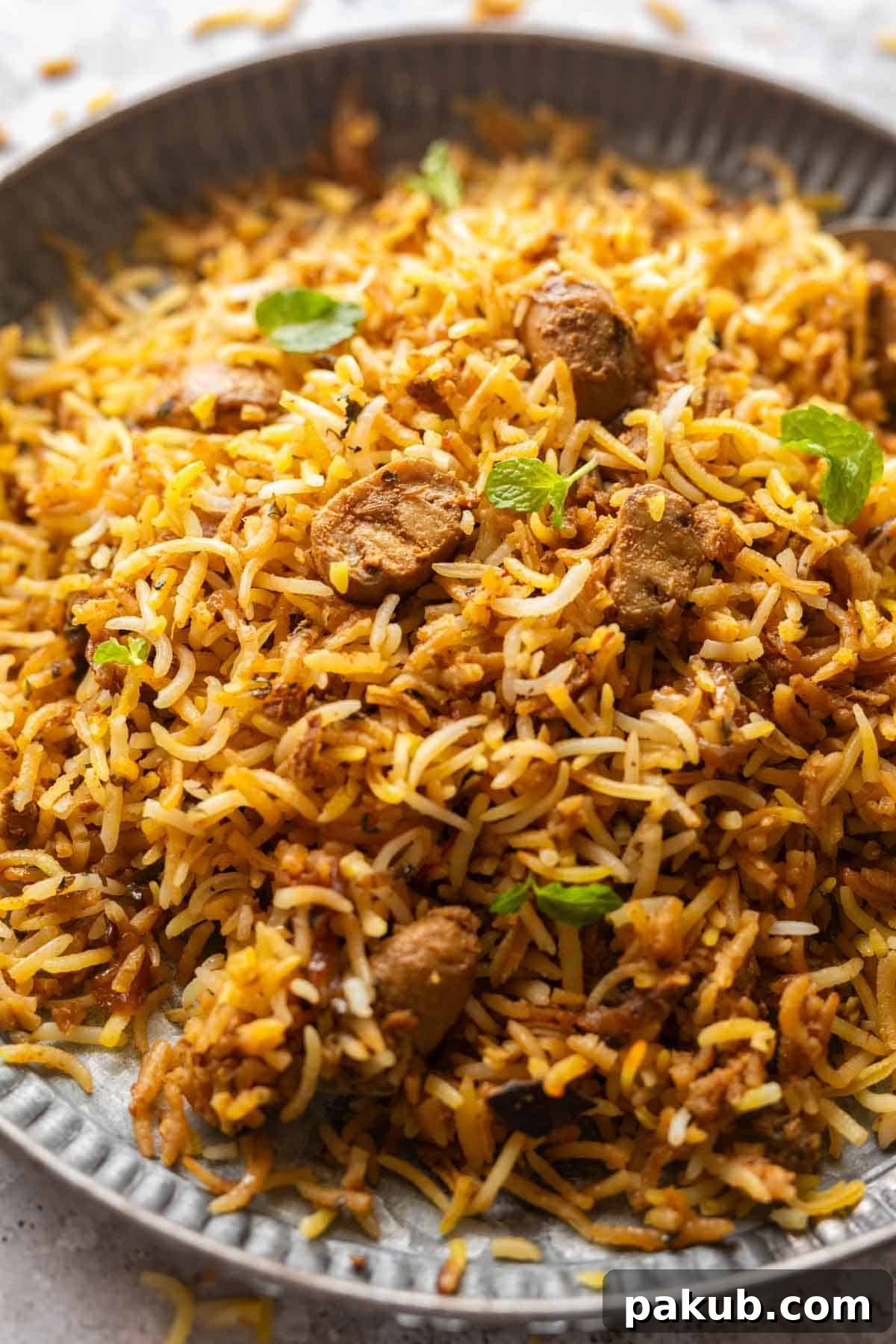 Aromatic Mushroom Biryani 3 Close up of a dish of mushroom biryani to show the fluffy texture of rice, separate grains of rice and pieces of mushrooms dotted all around it, garnished with fresh mint.