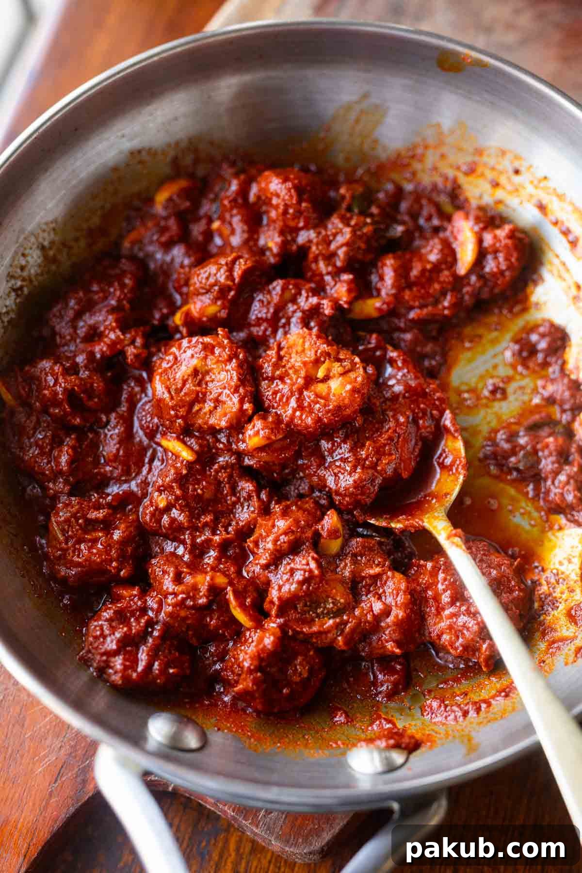 Prawn Pickle in a pan with a spoon showing a pickled prawn, highlighting its texture and succulence.