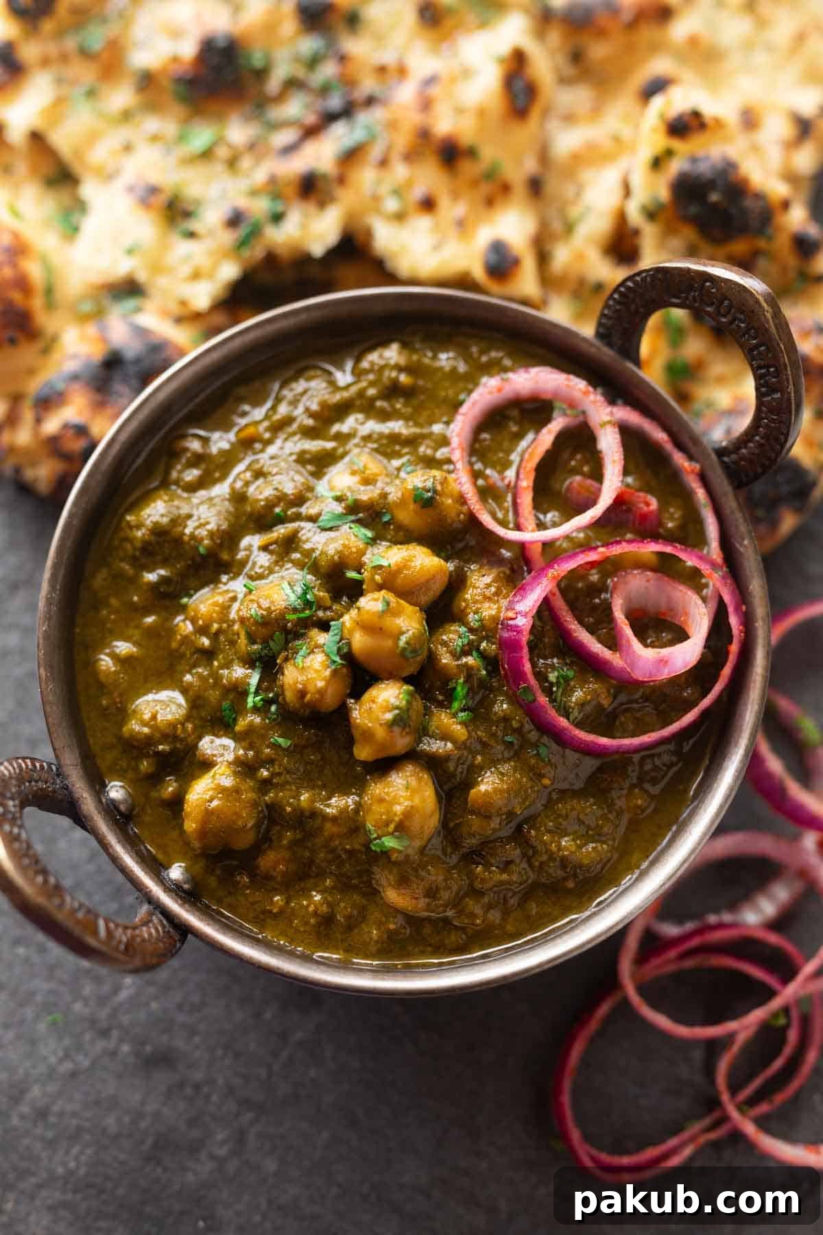 A beautifully presented bowl of vibrant green Spinach and Chickpea Curry (Chole Palak) served with fluffy garlic naan bread and fresh onion rings.
