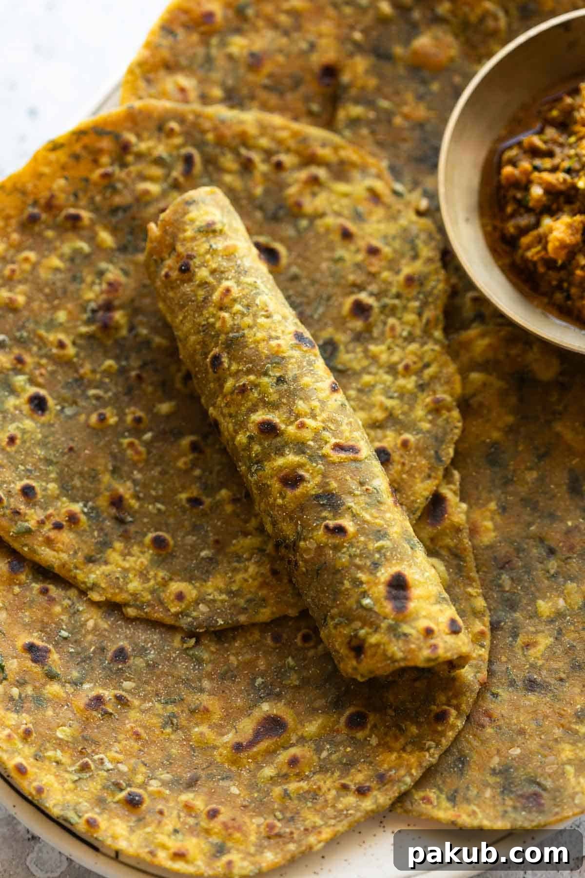 Soft and Spiced Methi Thepla 3 close up image of freshly made methi thepla with one rolled to showcase it's soft texture