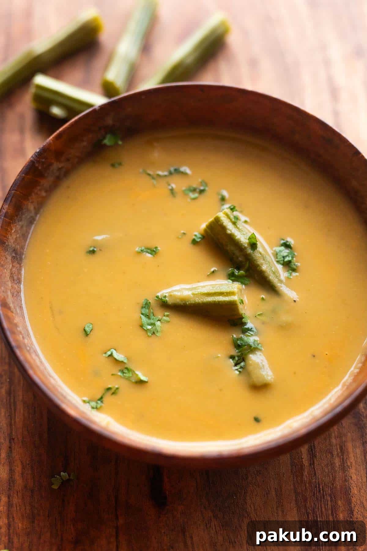 Nourishing Moringa Green Soup 2 drumstick soup served in a wooden bowl and garnished with boiled drumsticks and coriander leaves