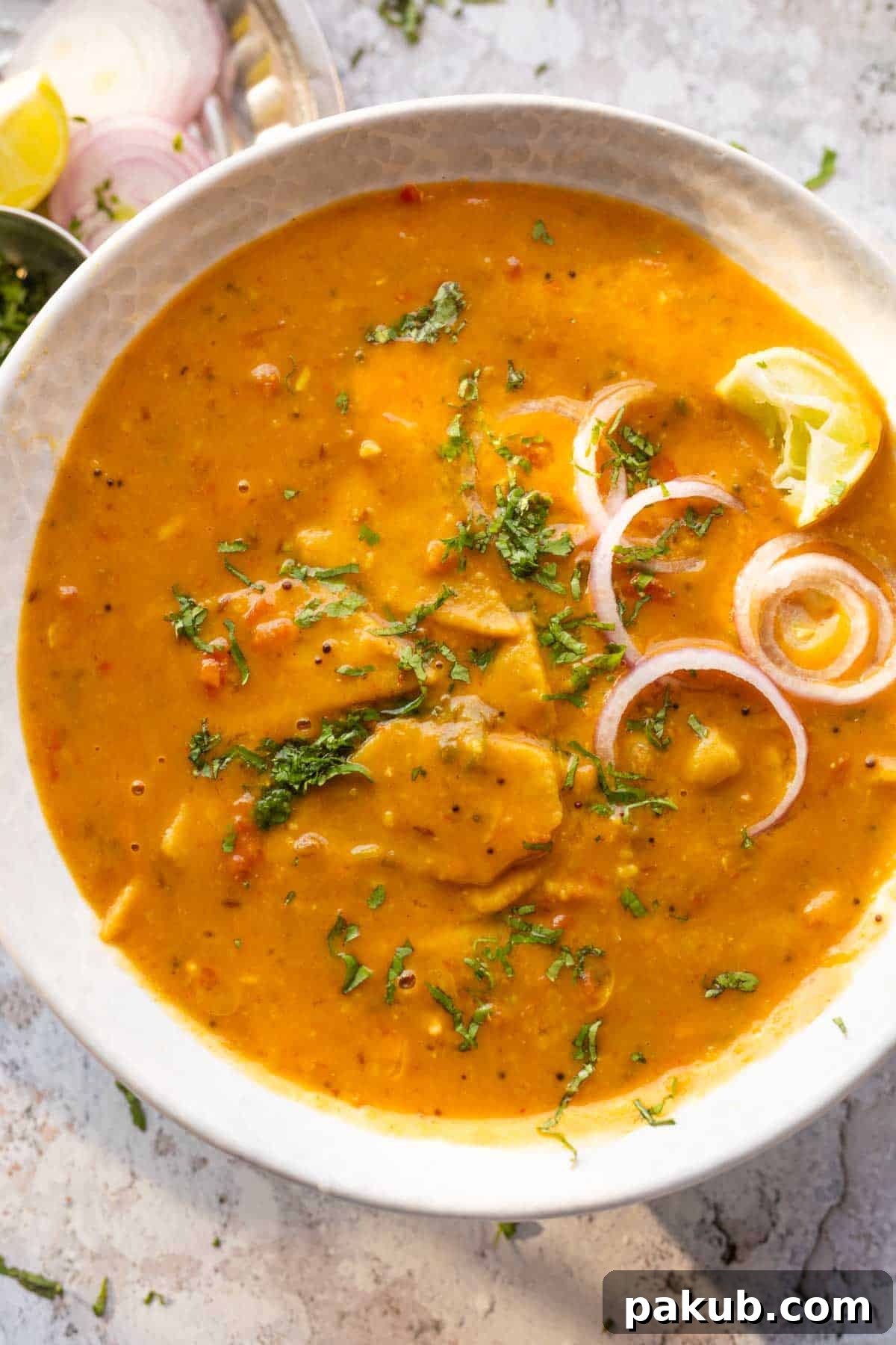 dal dhokli served in a bowl with onion rings and lemon wedges