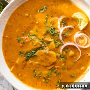 dal dhokli served in a bowl with onion rings and lemon wedges