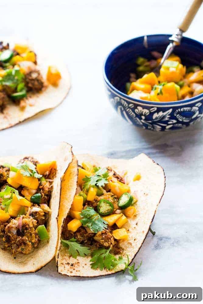 A close-up shot of a hand holding a perfectly assembled fish taco, highlighting the crispy fish, fresh mango salsa, and vibrant garnishes.