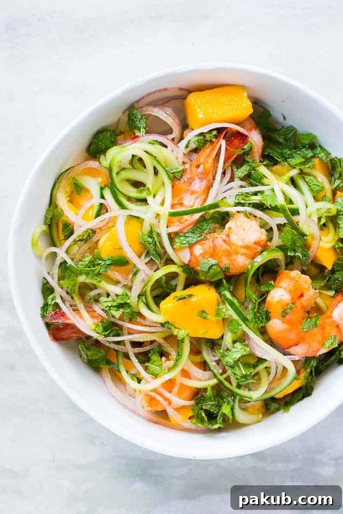 A vibrant cucumber noodle prawn and mango salad, beautifully arranged in a rustic bowl, showcasing its fresh ingredients and colorful appeal. Served chilled, ready to be enjoyed.