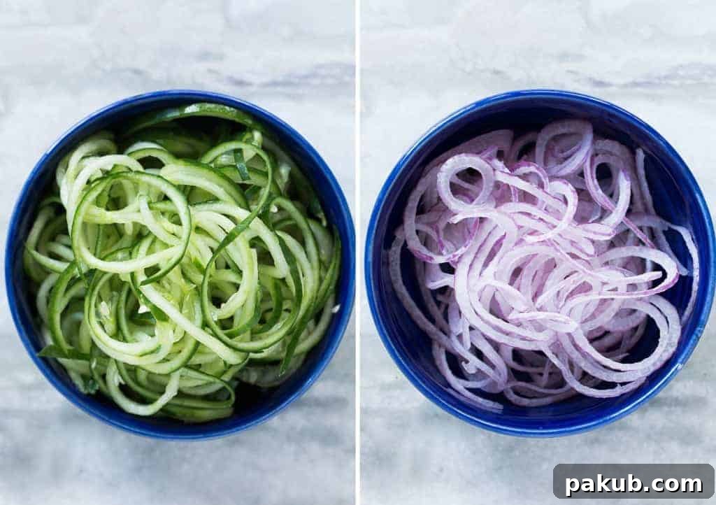 Finely spiralized cucumbers and thinly sliced red onions, prepared as vegetable noodles, ready to be incorporated into the salad.