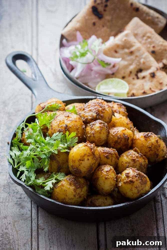 Mumbai's Zesty Potato Stir-Fry 2 A delectable serving of Bombay Potatoes garnished with fresh coriander in a rustic cast iron pan, accompanied by artfully sliced onions, a vibrant lemon wedge, and warm, fluffy rotis arranged on a side plate.