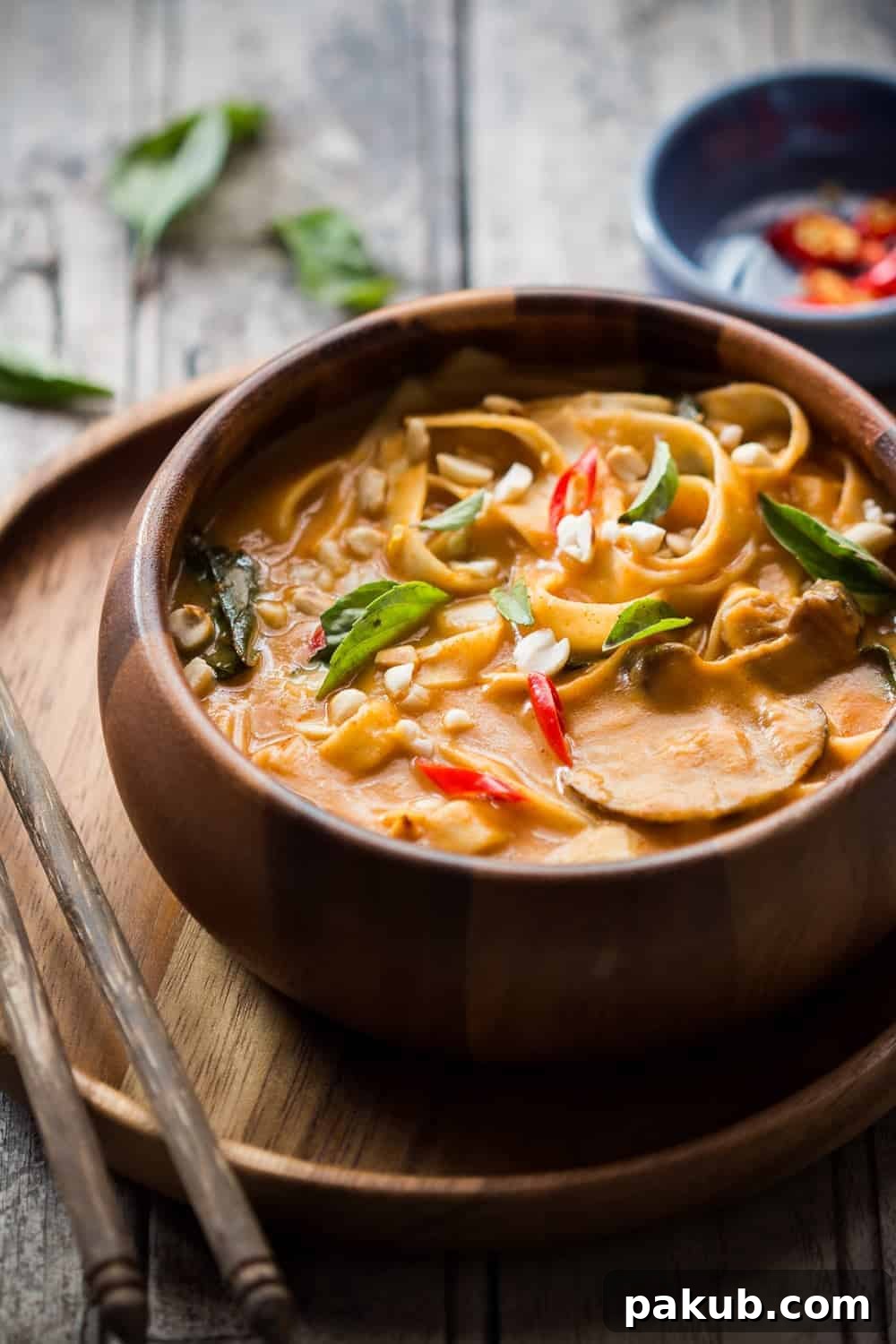 Comforting Thai Noodle Soup Close-up of spicy Thai curry pumpkin noodle soup in a rustic brown bowl, showcasing the rich broth, noodles, and mushrooms.