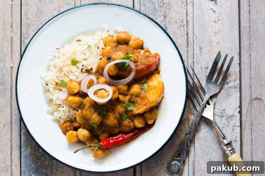 Chana Aloo Masala with Rice Chana Aloo Masala served with rice, sliced onions, and a green chili on a white plate, set on a brown wooden board.