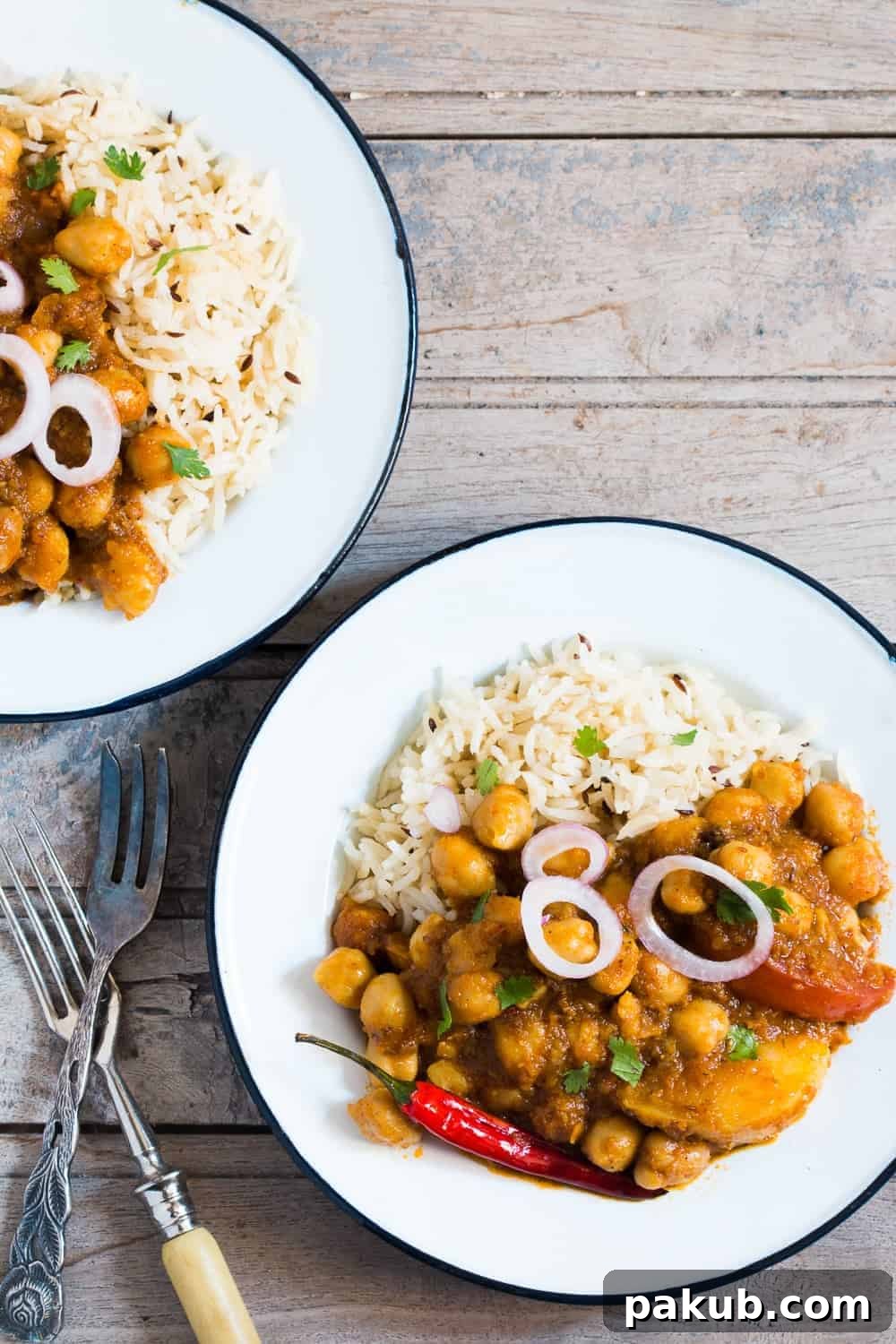 Chana Aloo Masala Platter Chana Aloo Masala served with fluffy rice, fresh cut onions, and a vibrant green chili on a white plate, placed on a rustic brown board.