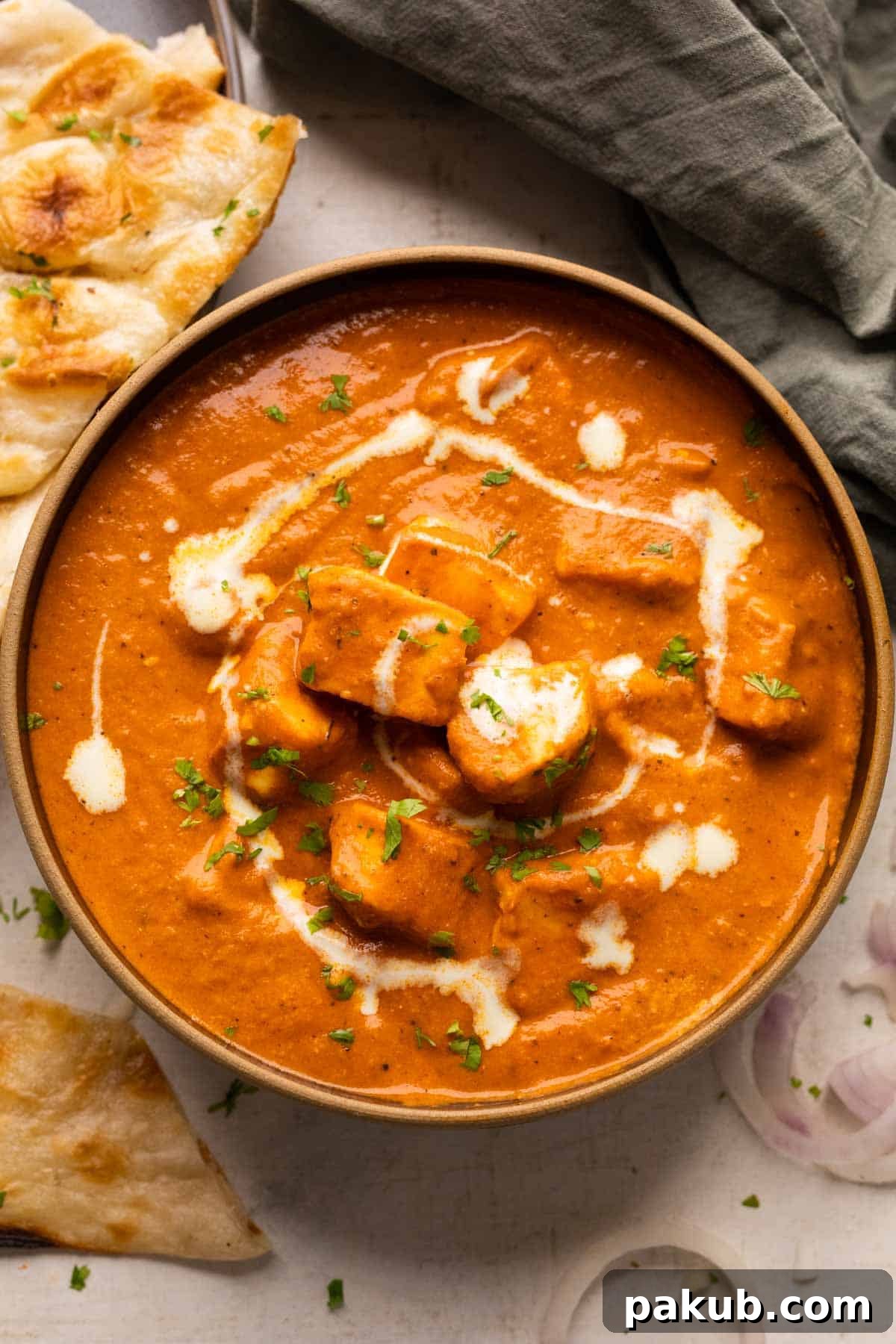 Creamy Restaurant Style Paneer Butter Masala 2 Paneer Butter Masala served in a black bowl with naan and sliced onions on the side