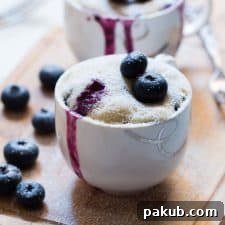 Close-up of an Eggless Blueberry Microwave Mug Cake with blueberries oozing, enticingly ready to be enjoyed.