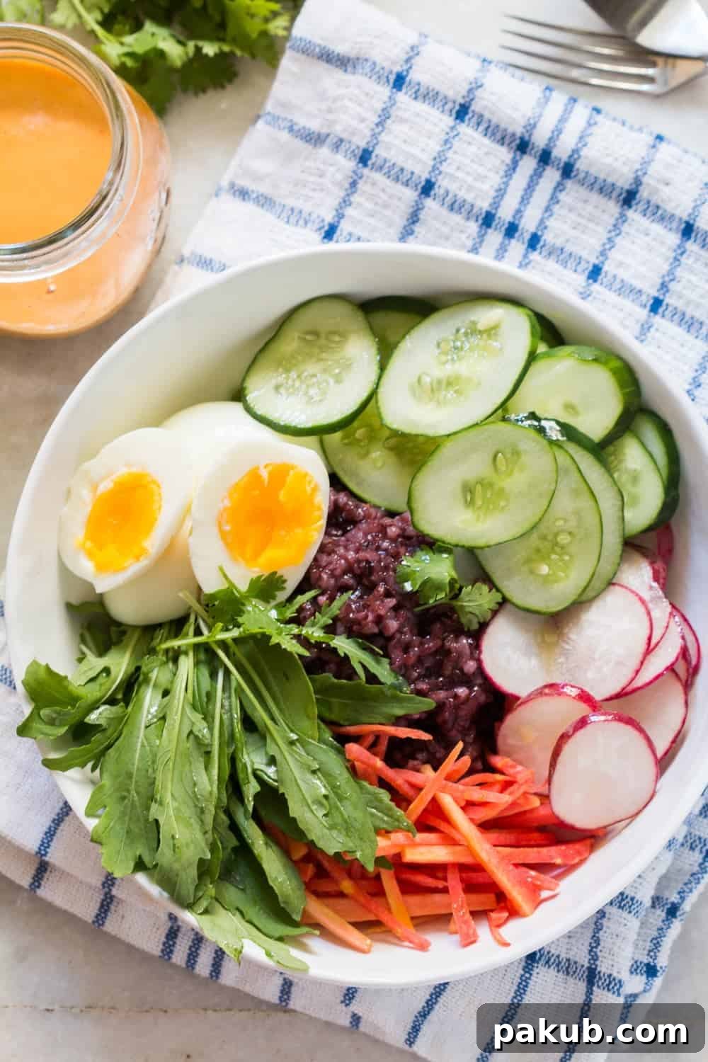 Prepared Black Rice Salad Bowl Top-down view of a generously portioned black rice salad bowl, showcasing all its colorful fresh ingredients. The bowl is placed on a blue and white patterned cloth, with a small jar of spicy peanut dressing neatly placed beside it.