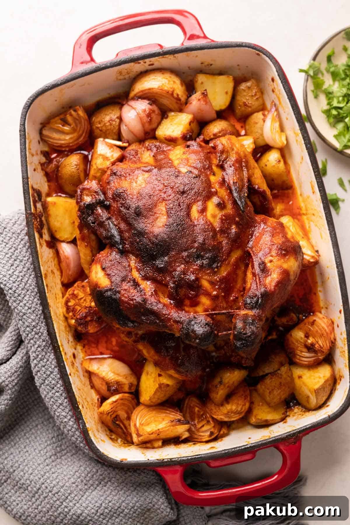 Indian roast chicken served on a bed of onions, potatoes and garlic in a red roasting pan