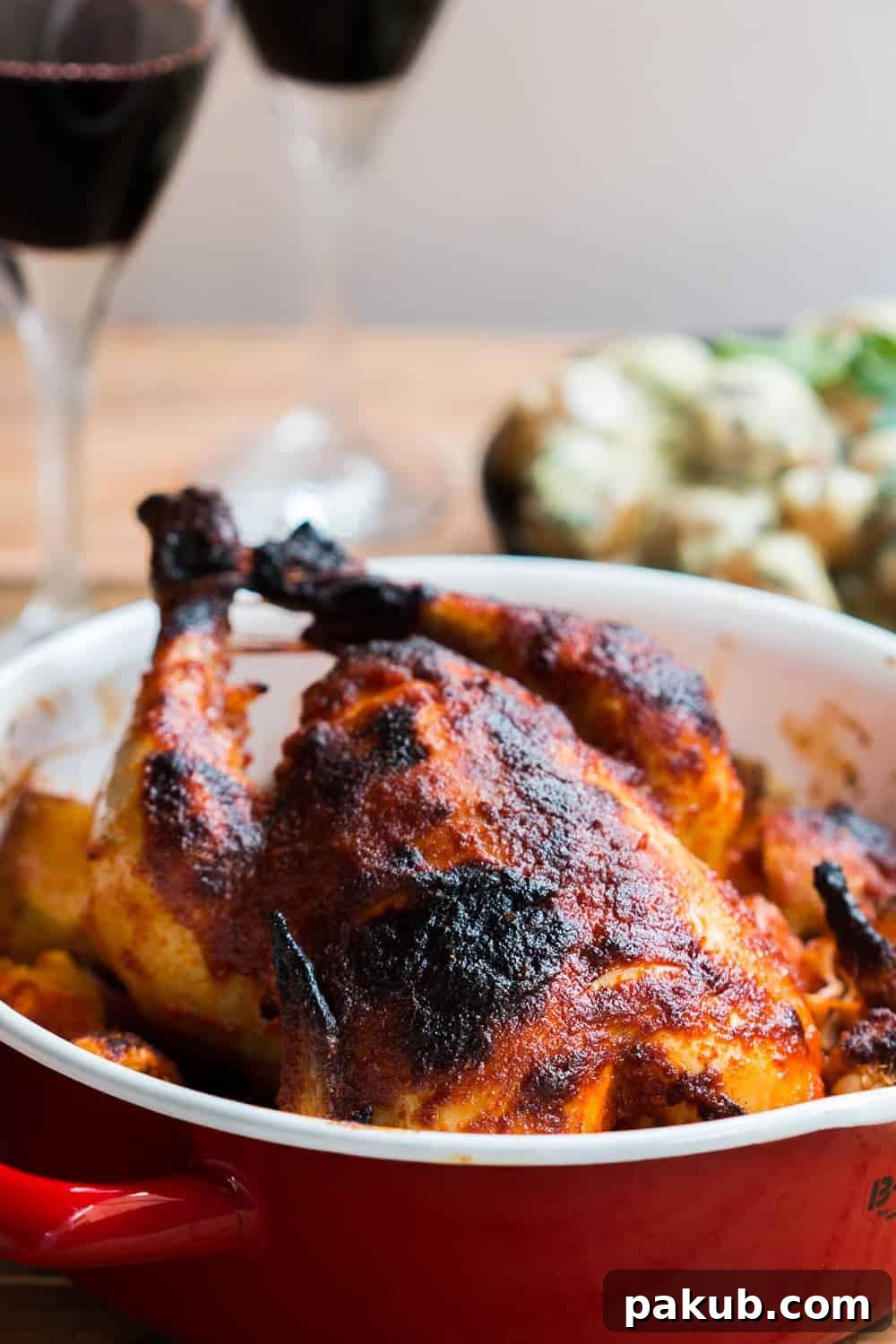 Indian roast chicken served on a bed of onions, potatoes and garlic in a red roasting pan
