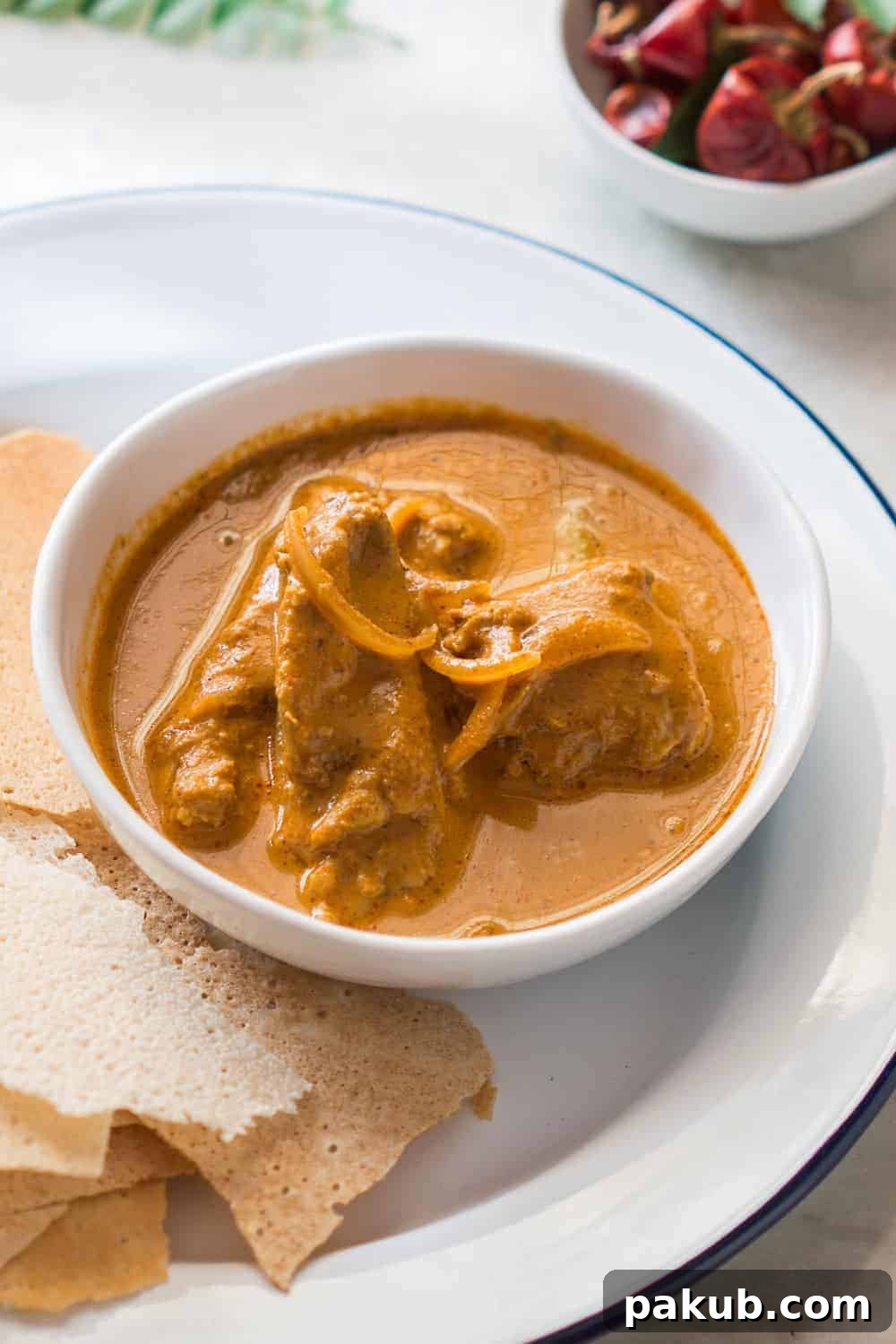 Mangalorean Kori Rotti Chicken Curry Rich Mangalorean chicken curry in a pristine white bowl, garnished with fresh coriander.