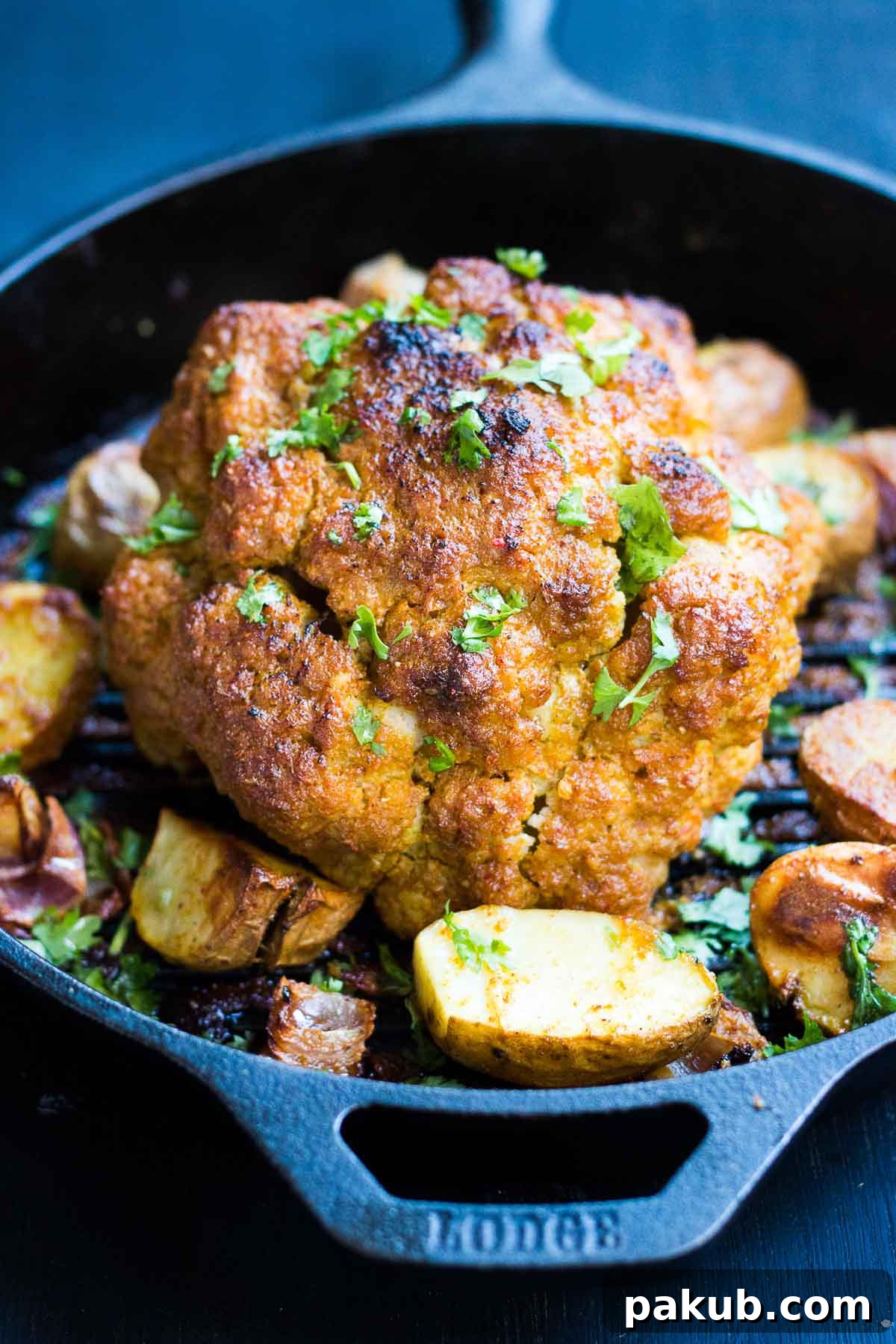 Tandoori Spiced Whole Roasted Cauliflower 2 A vibrant whole baked tandoori cauliflower, served with onions and potatoes in a rustic skillet, showcasing its golden color and charred edges.