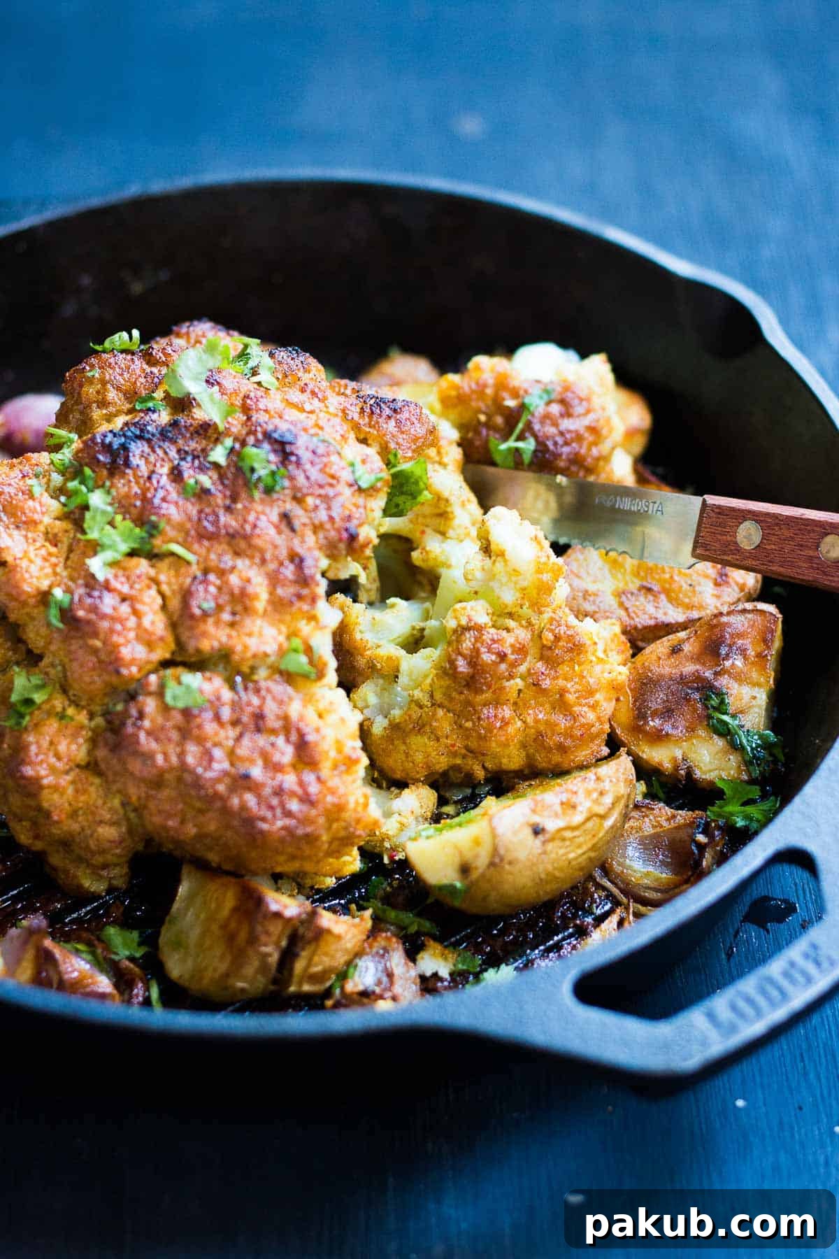 Tandoori Spiced Whole Roasted Cauliflower 3 Close-up of the tandoori cauliflower, highlighting its texture and spices, served with onions and potatoes in a skillet.