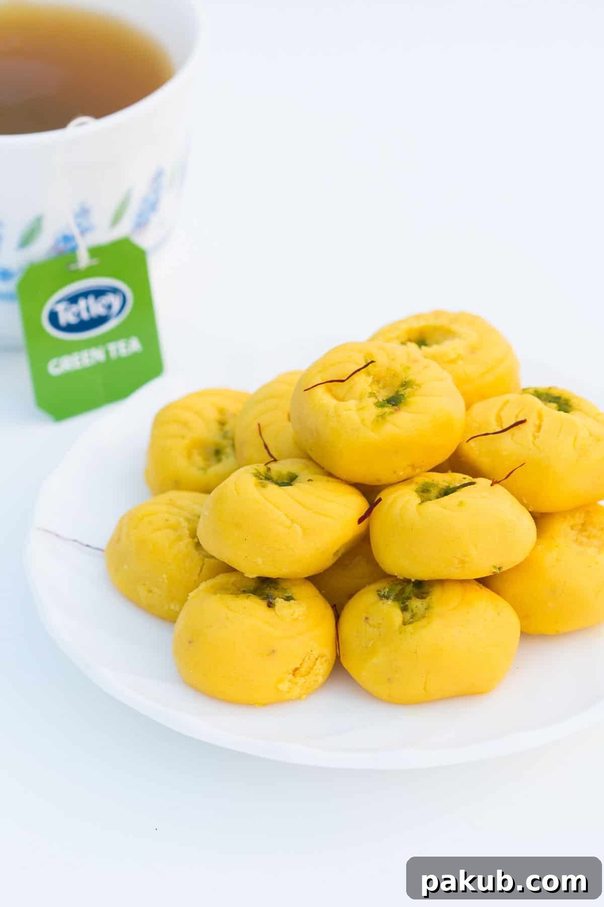 Simple Saffron Delights 2 Easy Kesar Pedas served on a white plate with a side of Tetley green tea.