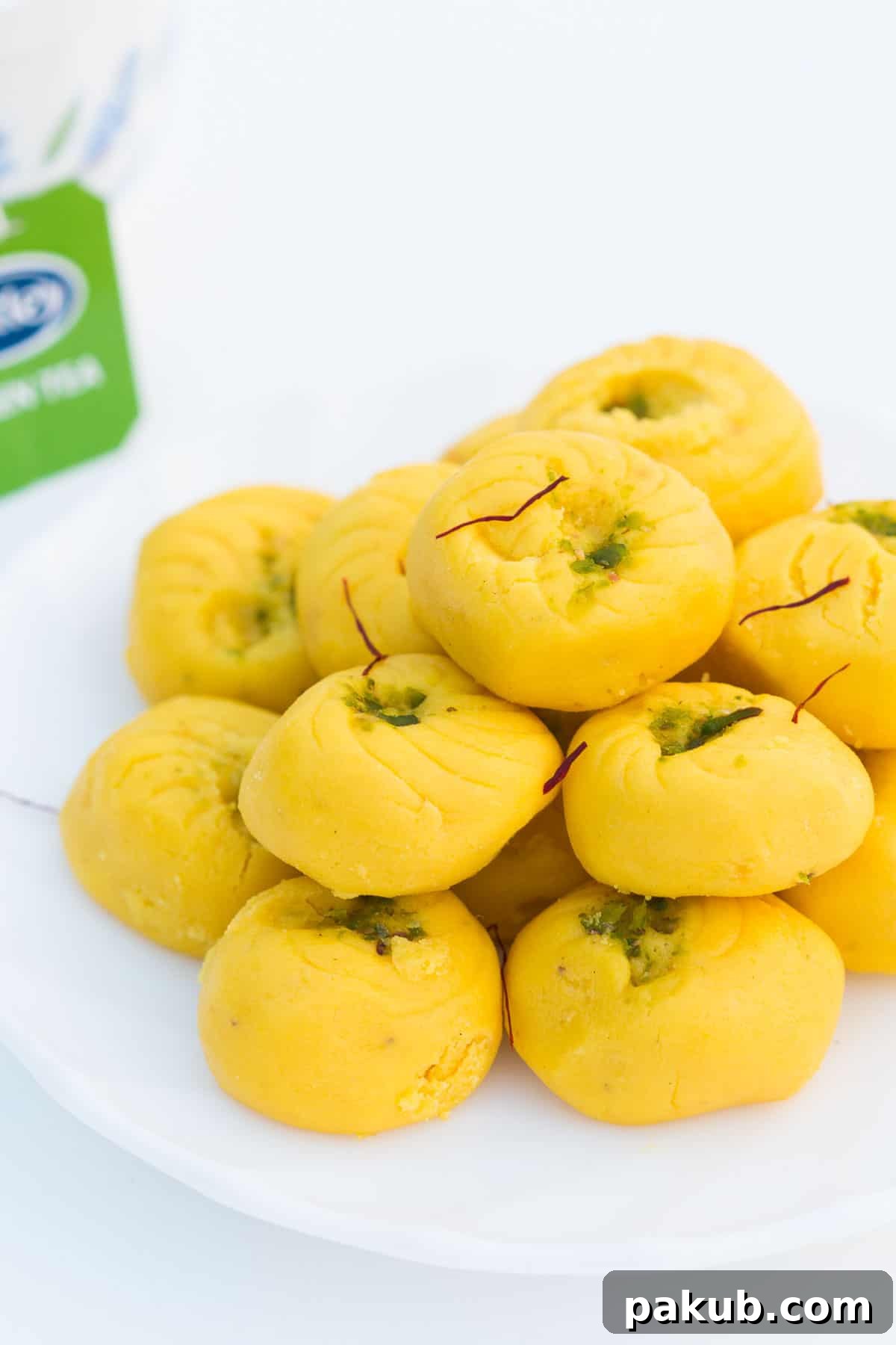 Simple Saffron Delights 3 Easy Kesar Pedas served on a white plate with a side of Tetley green tea.