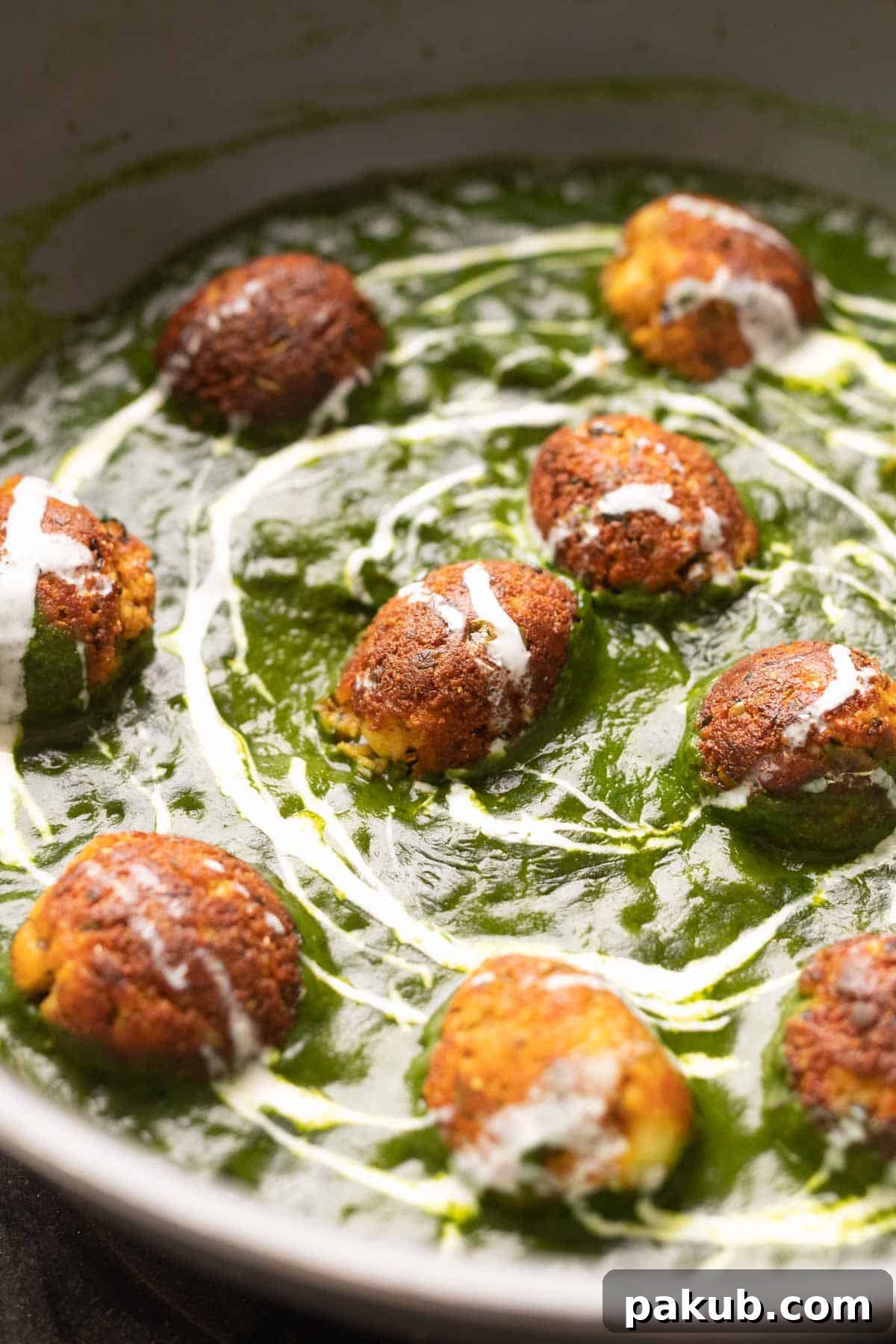 The Healthy Palak Paneer Kofta Curry in a pan with cream drizzled on top, showcasing a rich green color and golden koftas.