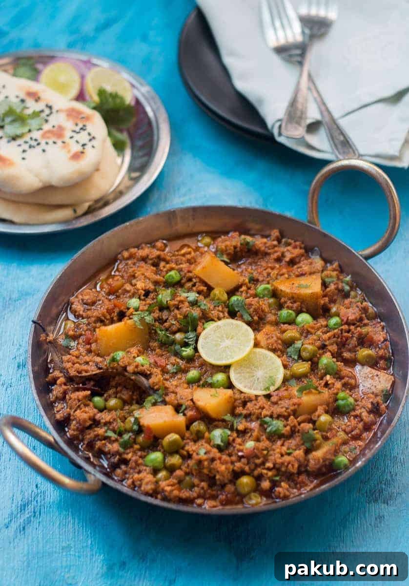 Keema in Kadhai Mutton Keema curry simmering in a traditional Indian kadhai, garnished with fresh limes, alongside chopped onions and warm naan bread