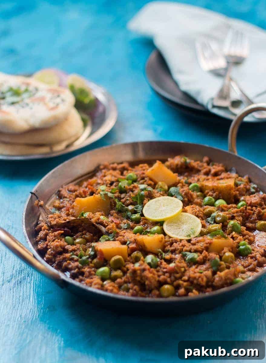 Spiced Lamb Mince Curry Close-up view of Mutton Keema curry in a kadhai, with garnishes of lime, onions, and naan bread visible on the side