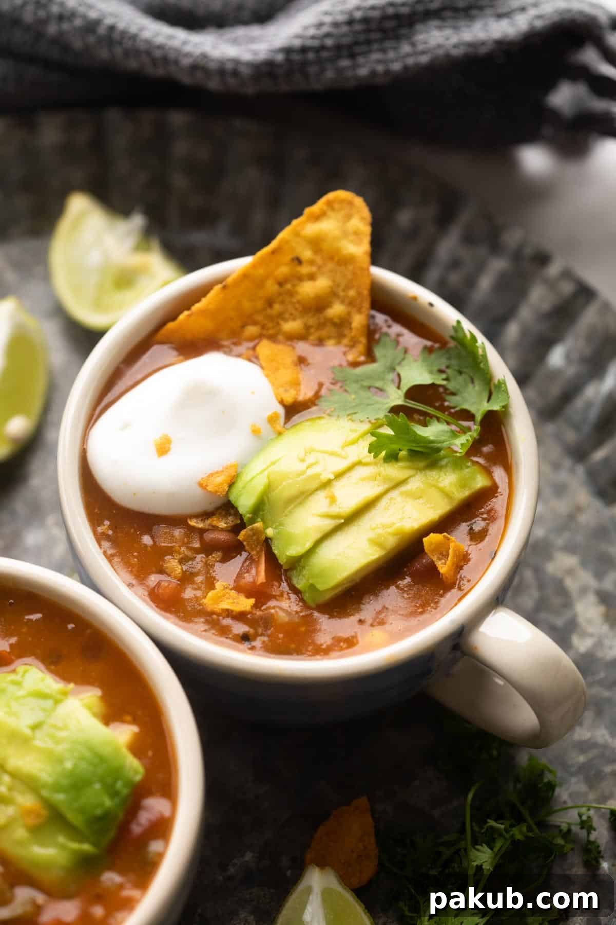 Mexican Plant-Based Bean Fiesta Soup 2 Picture of a steaming bowl of vegetarian Mexican soup, richly garnished with creamy avocado slices, fresh cilantro, a dollop of sour cream, and crunchy tortilla chips, ready to be enjoyed.