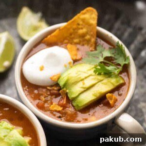 Picture of mexican soup served in a bowl topped with avocado, cilantro, sour cream and tortilla chips