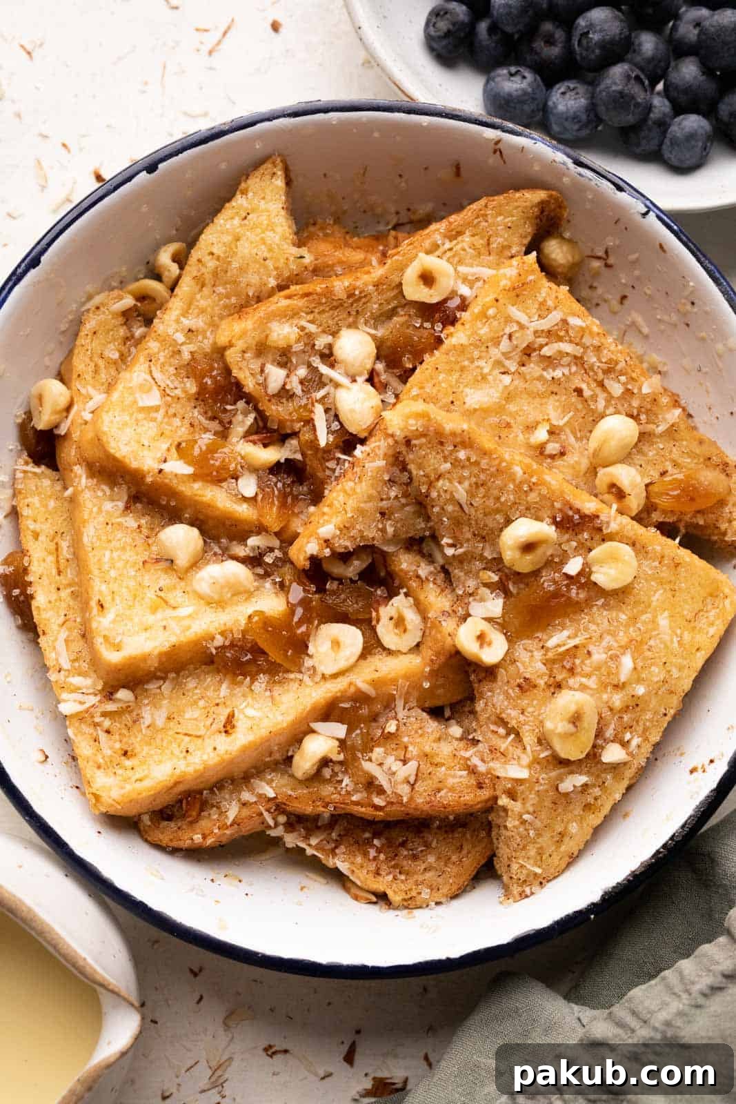 Golden-brown cinnamon bread pudding brushed with melted butter, served in a round enamel baking dish, garnished with fresh blueberries and a side of creamy rum custard sauce.
