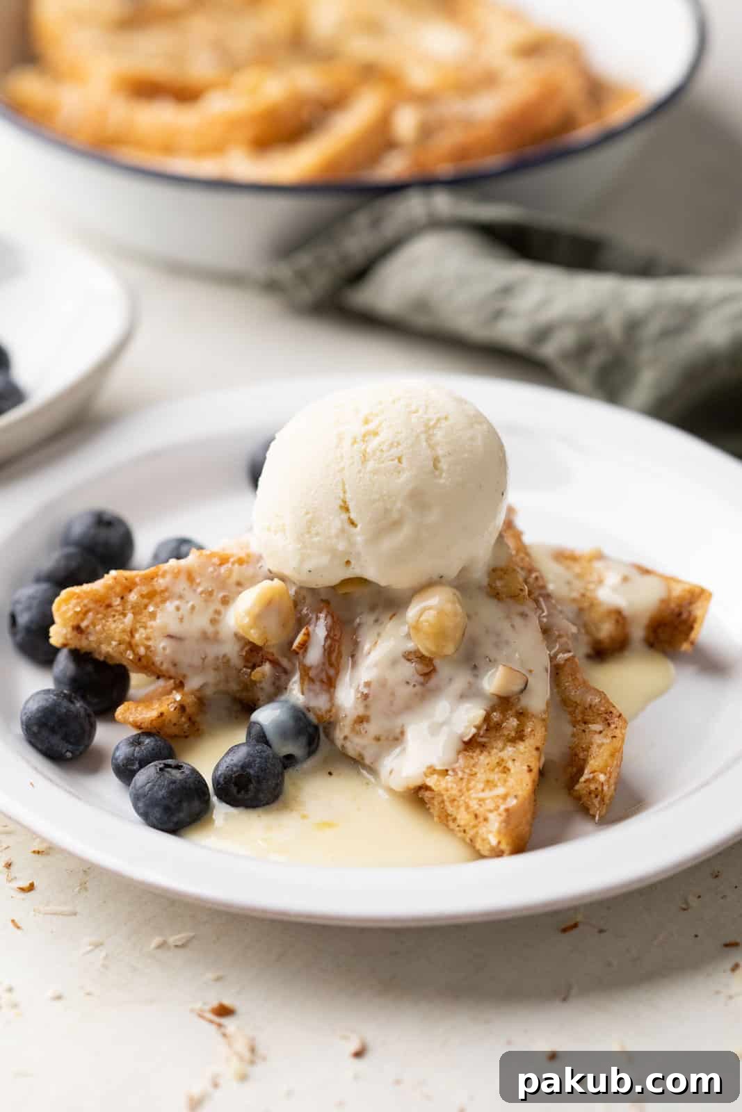 A serving of cinnamon bread pudding on a white plate, generously topped with a rich rum custard sauce and a scoop of vanilla ice cream, creating a perfect balance of warm and cold.