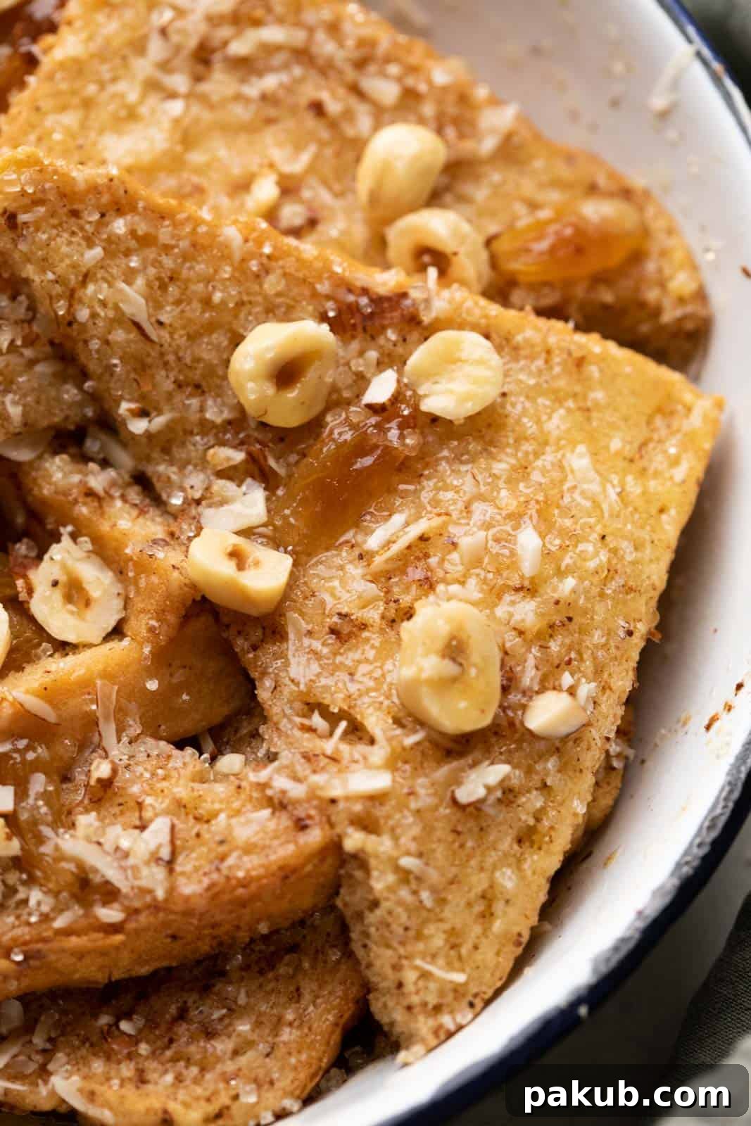 A close-up shot of a slice of cinnamon bread pudding, highlighting its beautiful, moist texture glistening with melted butter and topped with crunchy nuts and sweet raisins.
