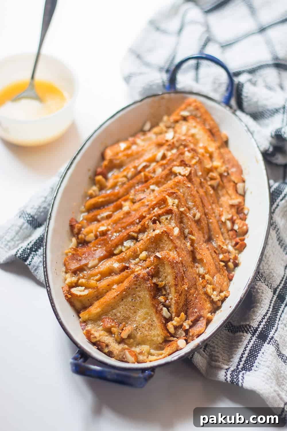 An older image displaying cinnamon bread pudding layered in an oval dish, resting on a blue and white checkered cloth, showing an alternative presentation style.