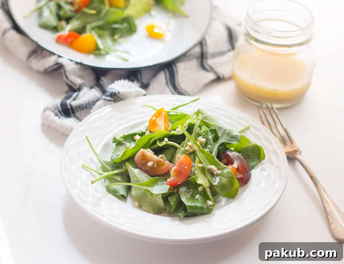 Spinach, Heirloom Tomato and Crumbled Tofu Salad with Roasted Garlic Dressing served in a white bowl, showcasing vibrant colors and fresh ingredients.
