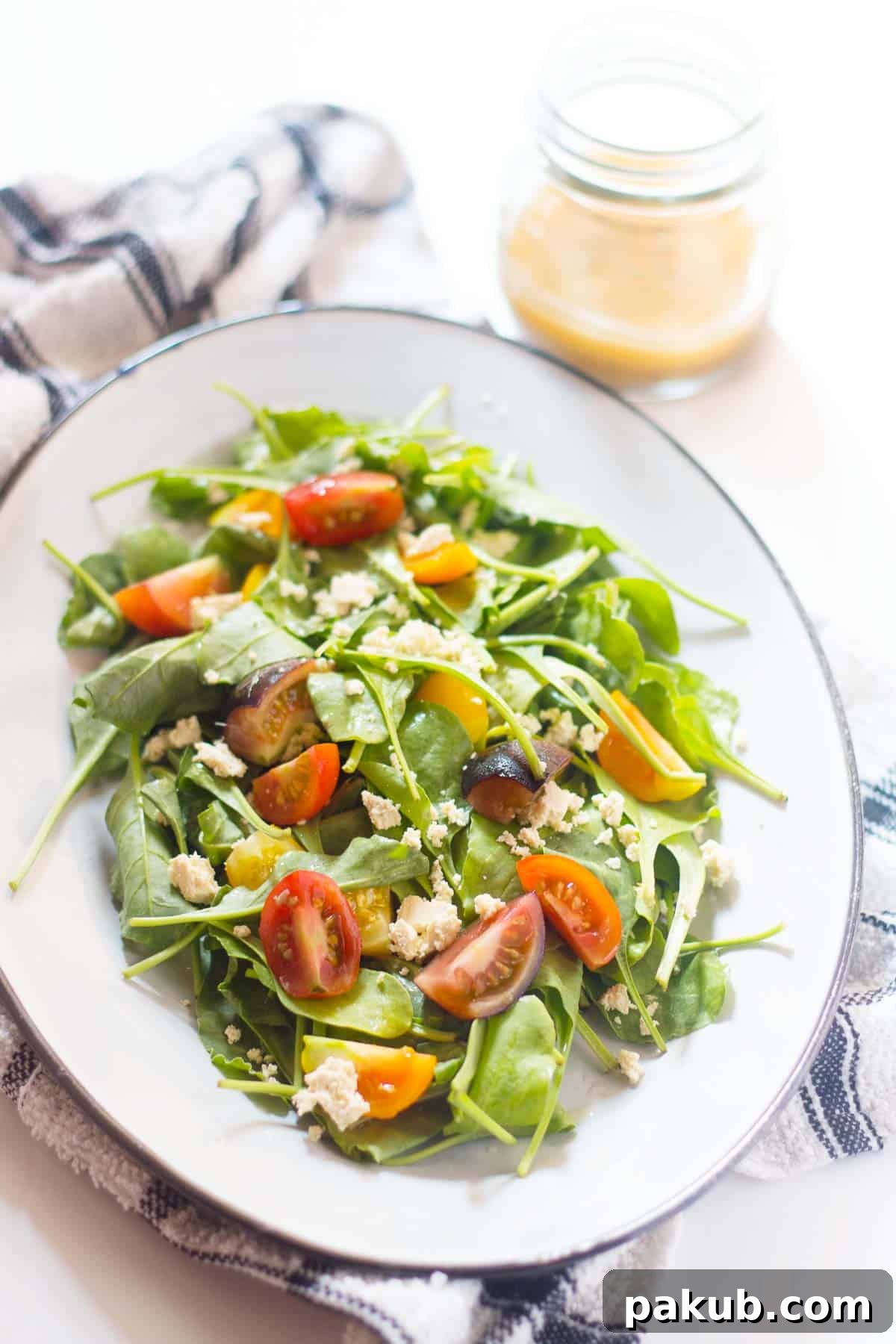 Spinach, Heirloom Tomato and Crumbled Tofu Salad with Roasted Garlic Dressing served on a pristine white plate, with extra dressing in a small side bowl for customization.