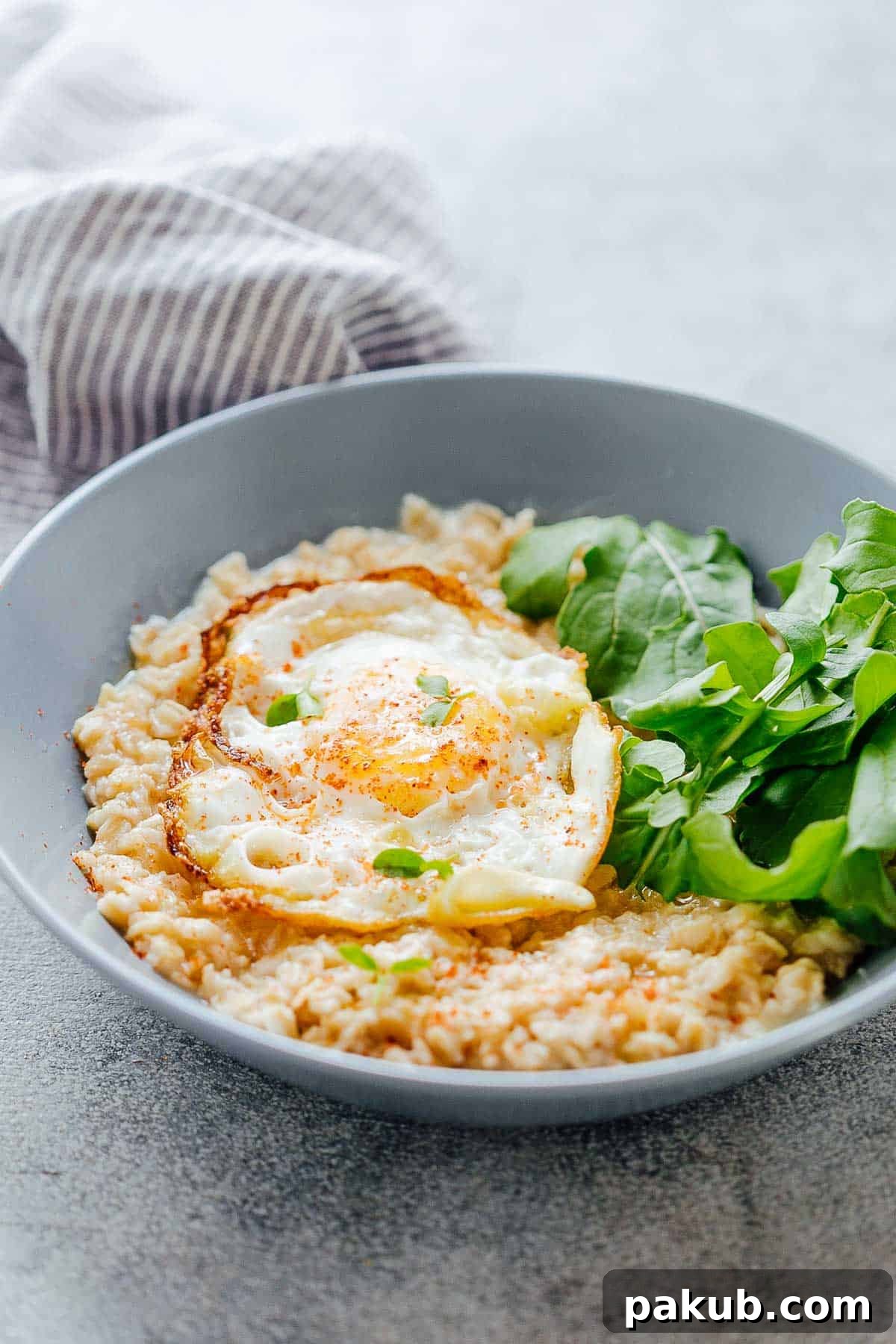 Umami Garlic Oats with Golden Masala Egg 2 Savory Garlic Oats with Masala Fried Egg in a bowl with mixed lettuce greens