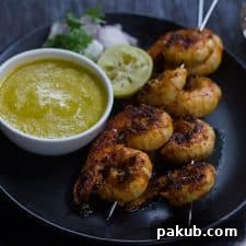 Tandoori Prawns served with mango chutney, onions and lemon in a black plate.