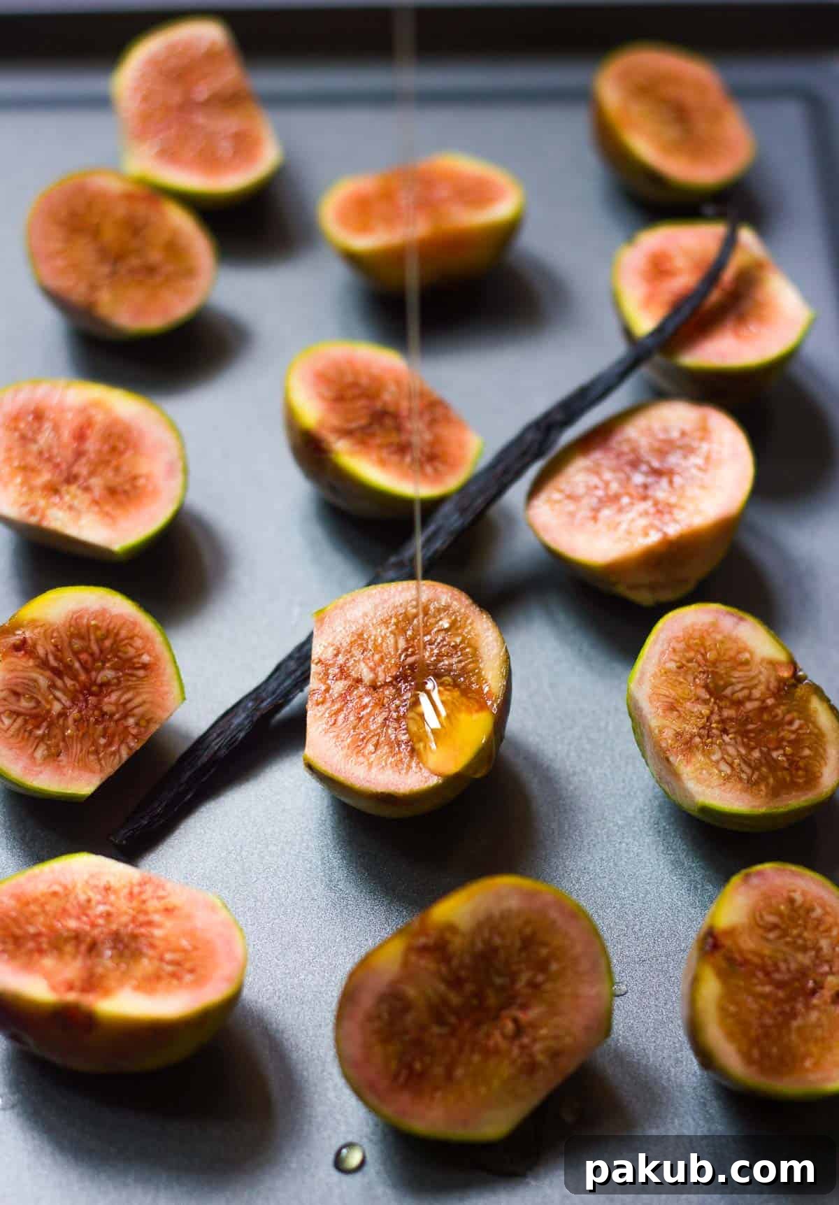 Golden honey being generously drizzled over halved fresh figs arranged on a parchment-lined baking sheet, preparing them for the roasting process.
