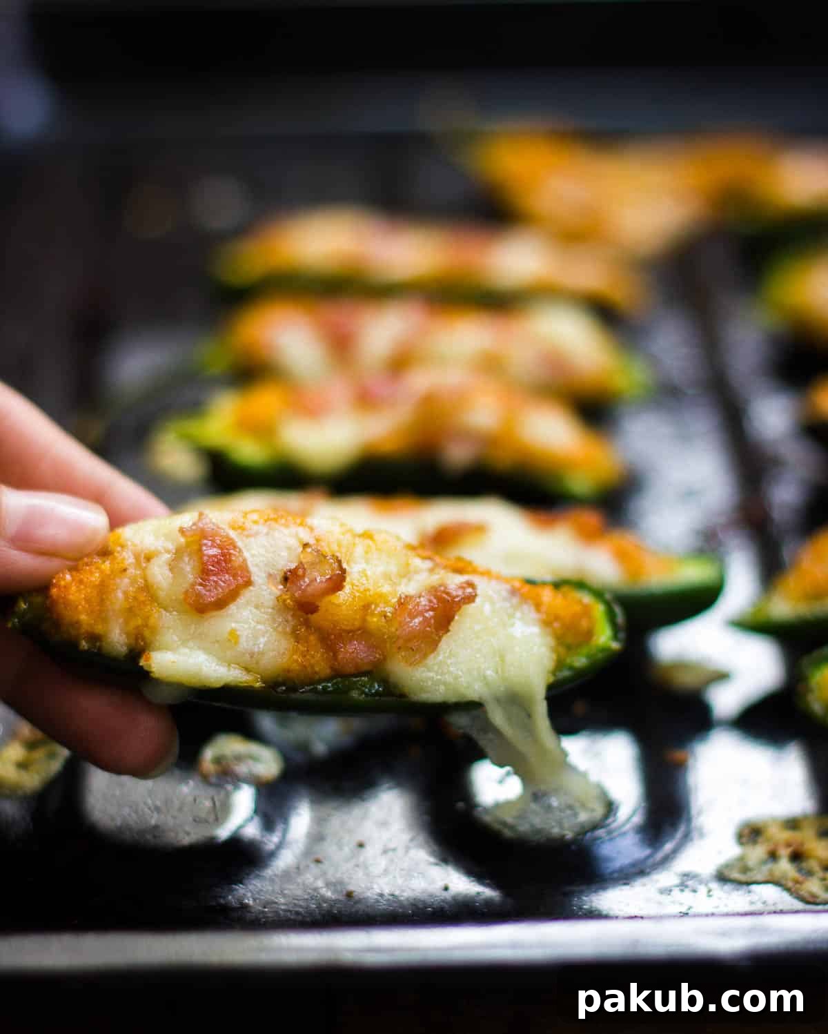 Oven Baked Cottage Jalapeno Delights 5 A hand gracefully picking up a warm, golden baked jalapeno popper from a dark serving tray, highlighting its inviting texture.