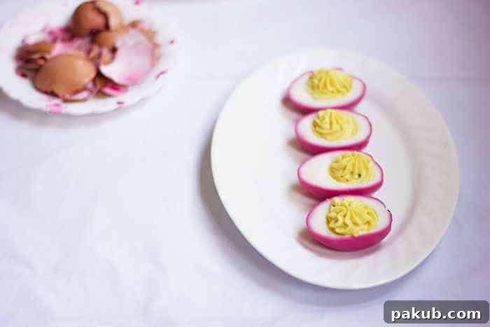 Naturally dyed pink eggs, some with cracked shells, on a white plate, highlighting their organic beauty.