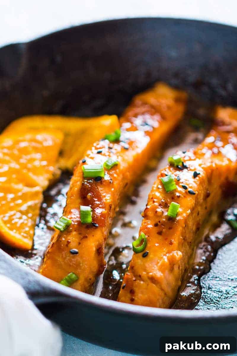 Sizzling Salmon with Orange-Mustard Glaze 4 Three golden-brown pan-seared salmon fillets bathed in orange mustard sauce, garnished with sesame seeds and ready to be served, highlighting their inviting texture.