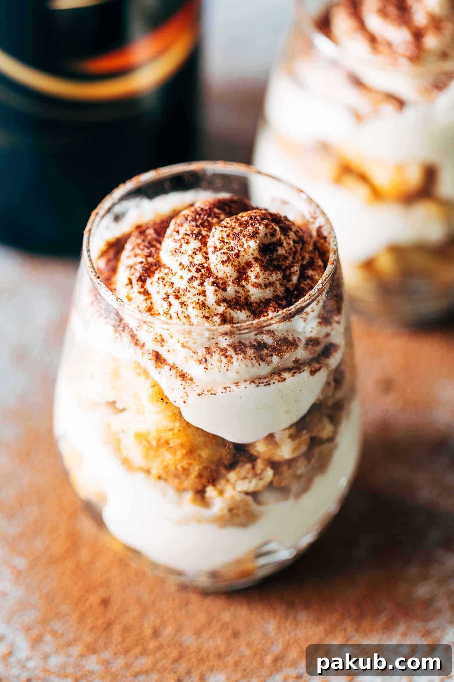 Close-up of a Baileys Tiramisu Trifle Cup, showing layers of coffee-soaked ladyfingers and whipped cream, dusted with cocoa powder for an inviting finish.