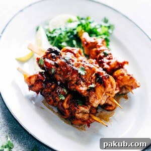 Grilled Sambal Chicken Skewers served with lemon slices and coriander on a white plate.