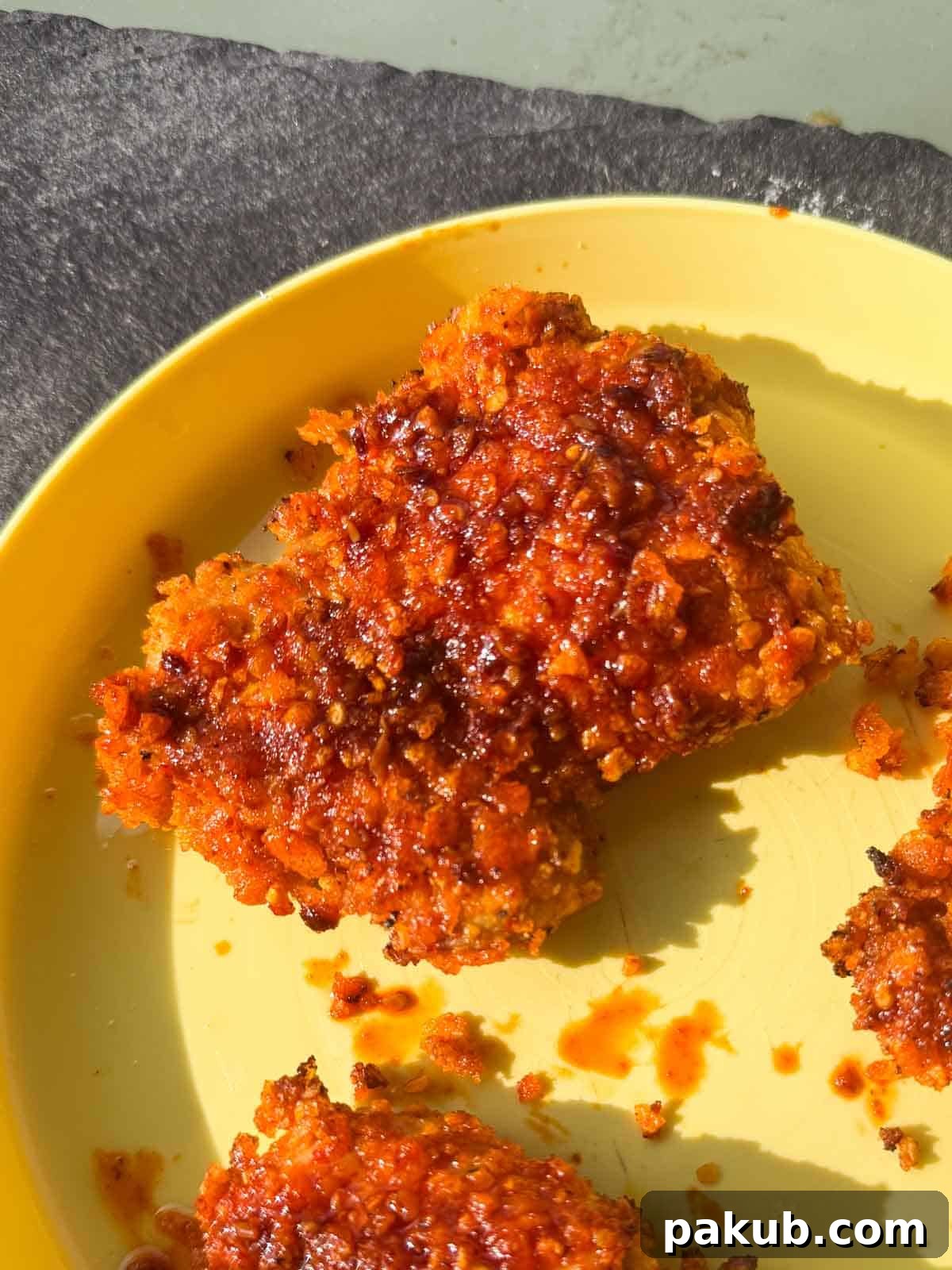 Two generous pieces of perfectly air-fried Nashville hot chicken, glistening with fiery oil, presented on a rustic plate alongside fresh garnishes, creating an enticing and mouth-watering display.