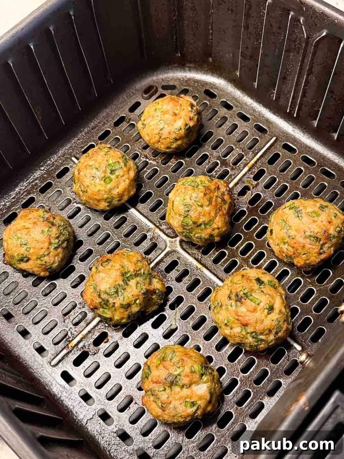 A close-up shot of freshly cooked chicken meatballs still in the air fryer basket, showcasing their perfectly golden-brown and slightly crispy exterior.