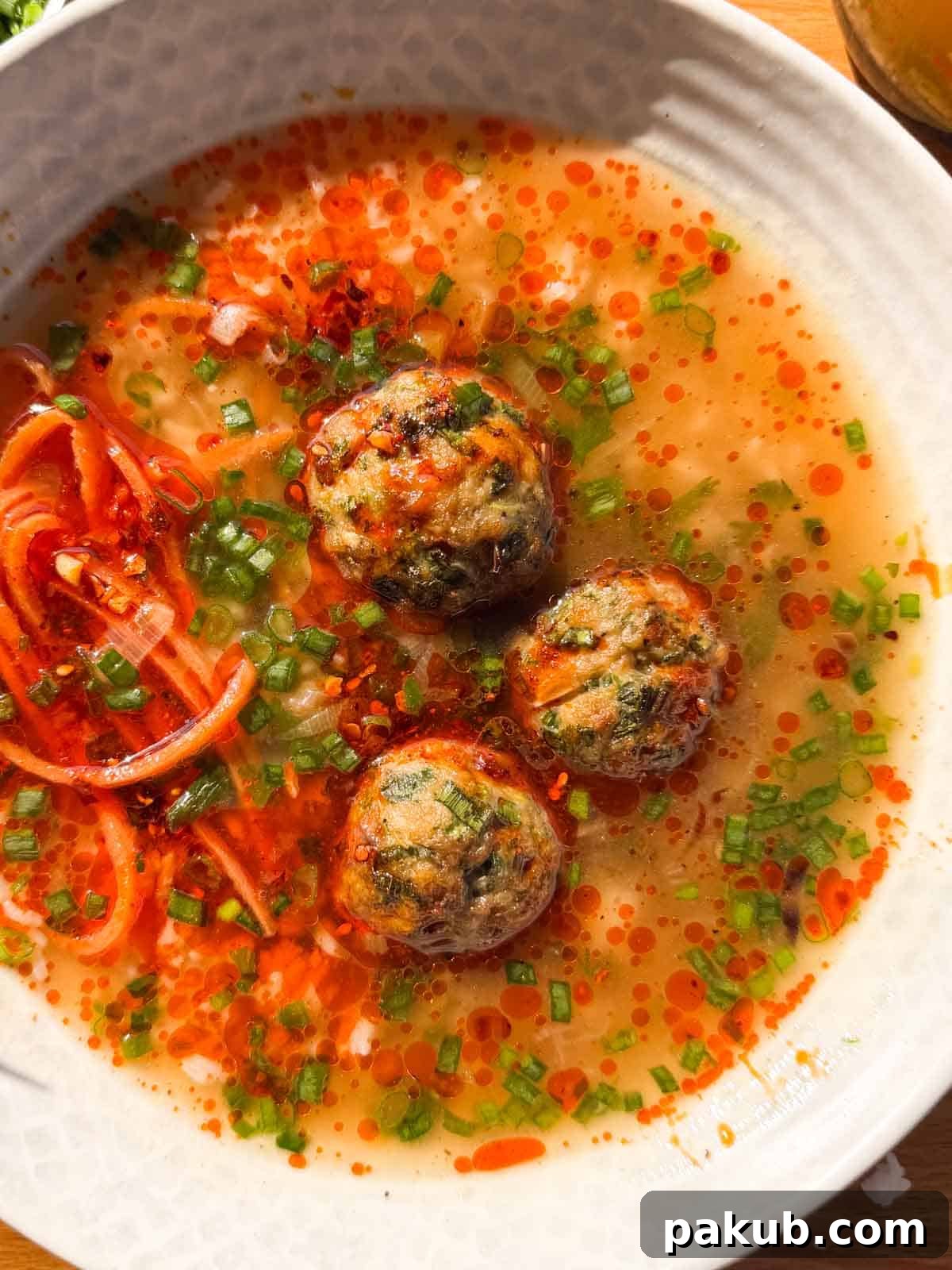 An inviting close-up image of a bowl of Asian chicken meatballs in ginger broth, showcasing the vibrant colors and appealing textures of the dish.